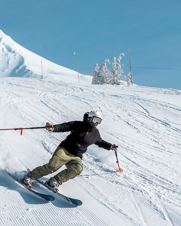 Skier carving down a snowy slope at Timberline Lodge with Mount Hood’s sunlit peak in the background.