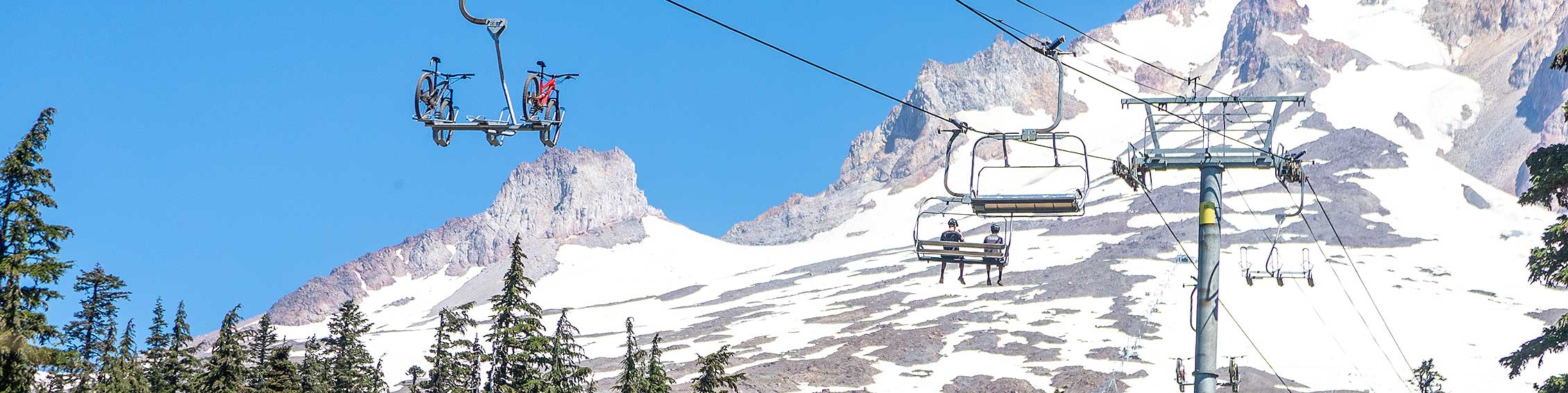 MOUNTAIN BIKERS AND THEIR BIKES RIDING THE LIFT AT THE TIMBERLINE BIKE PARK WITH MT. HOOD LARGE IN THE BACKGROUND