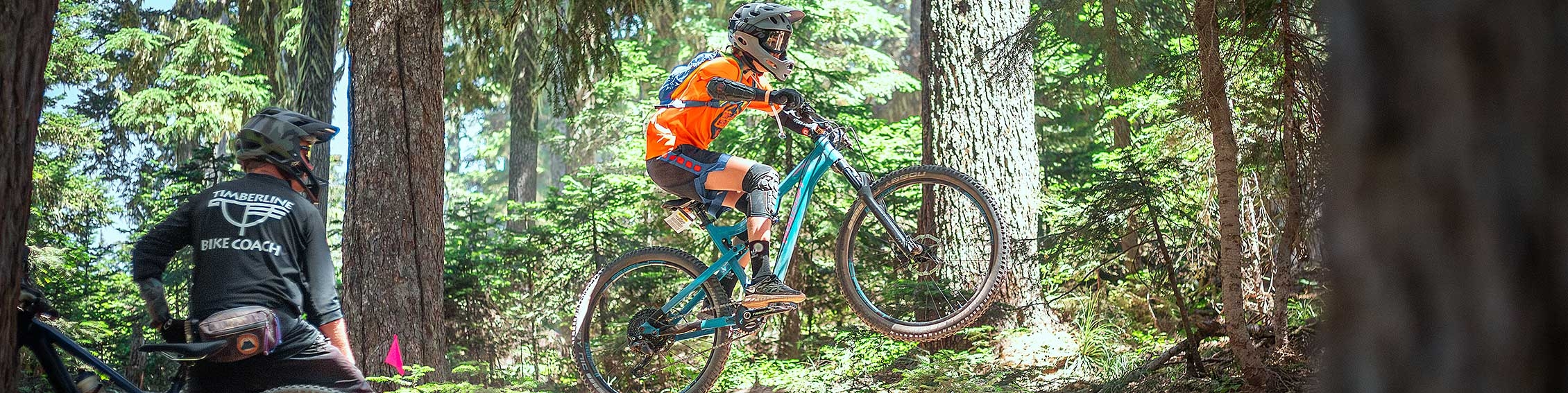 TIMBERLINE BIKE PARK COACH WITH STUDENT JUMPING THEIR MOUNTAIN BIKE IN THE BIKE PARK ON MT. HOOD