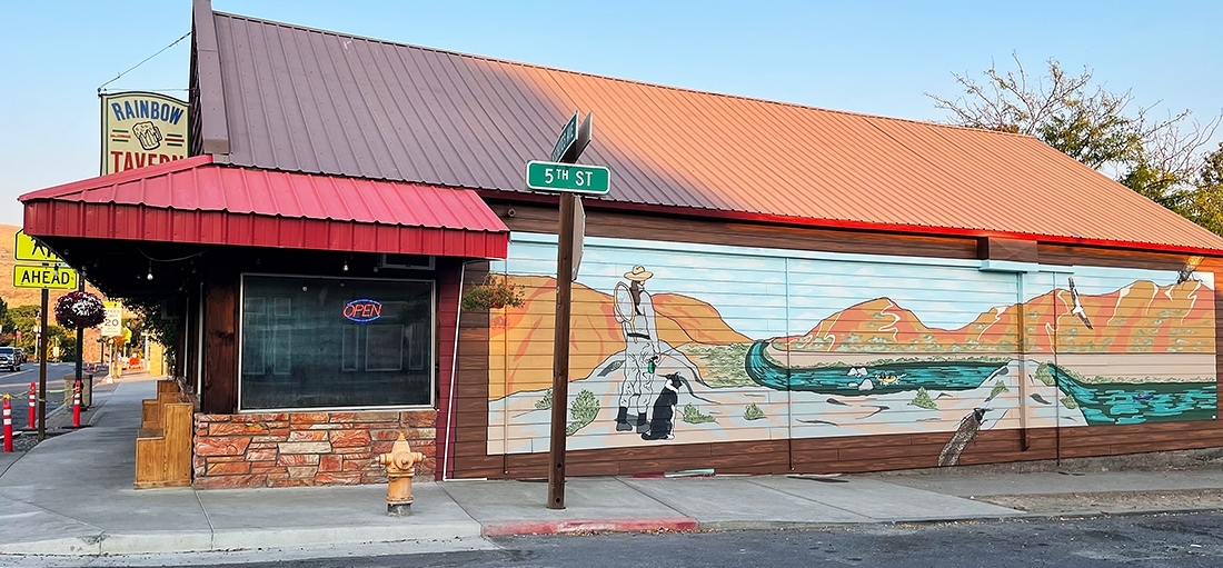 EXTERIOR PHOTO OF THE RAINBOW TAVERN IN MAUPIN, OR, SHOWING A COLORFUL MURAL OF A FLY FISHERWOMAN AND HER DOG LOOKING AT THE DESCHUTES RIVER