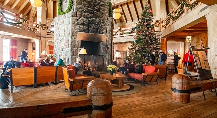 TIMBERLINE MAIN HEADHOUSE PHOTO SHOWING HUGE FIREPLACE WITH PEOPLE SITTING ON COUCHES NEAR 30' TALL DECORATED CHRISTMAS TREE