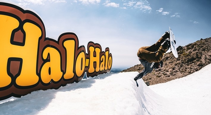 SNOWBOARDER UPSIDE DOWN ON SNOW LIP IN FRONT OF HALO-HALO SIGN AT TIMBERLINE ON MT. HOOD