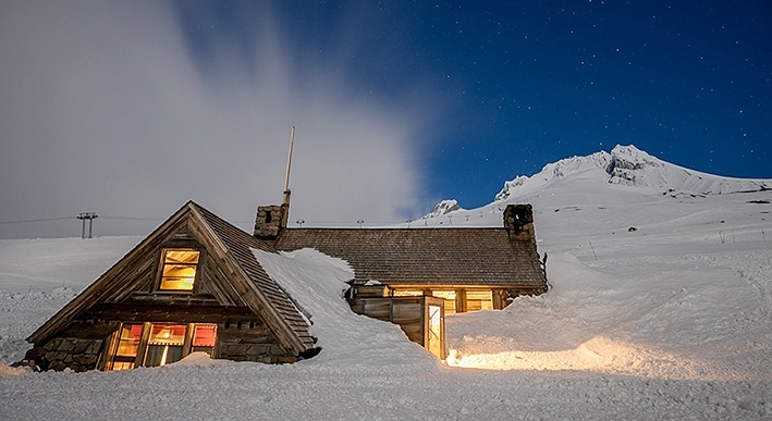 SILCOX HUT LIT UP AT DUSK WITH WHISPY CLOUDS AND SNOWY MT HOOD IN THE BACKGROUND