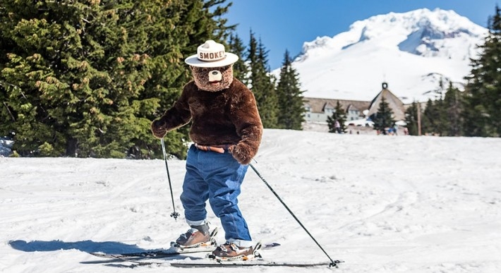 Smokey Bear on skis in the snow in front of Timberline Lodge and Mt. Hood
