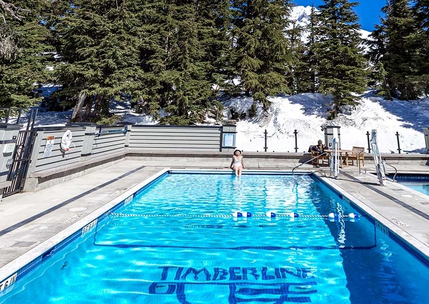 Women sitting at far end of the Timberline swimming pool with fir trees and Mt. Hood in the background