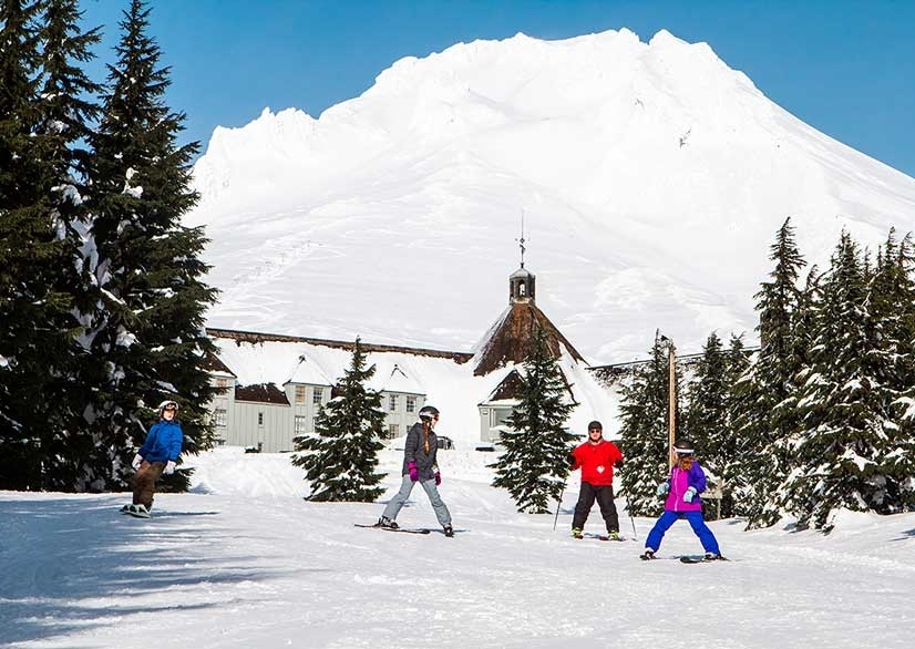 Family of four skiing and snowboarding in front of Timberline Lodge on Mt. Hood