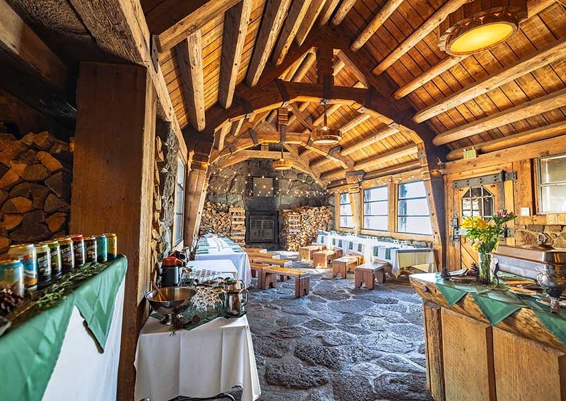 Interior of Silcox Hut, a rustic mountain lodge with exposed timber beams, stone floors, and wooden furniture. 
