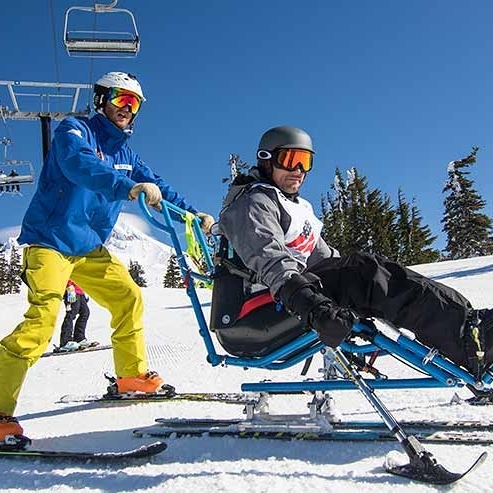 ADAPTIVE SKIER BEING PUSHED BY PERSON ON SKIS IN FRONT OF MT. HOOD