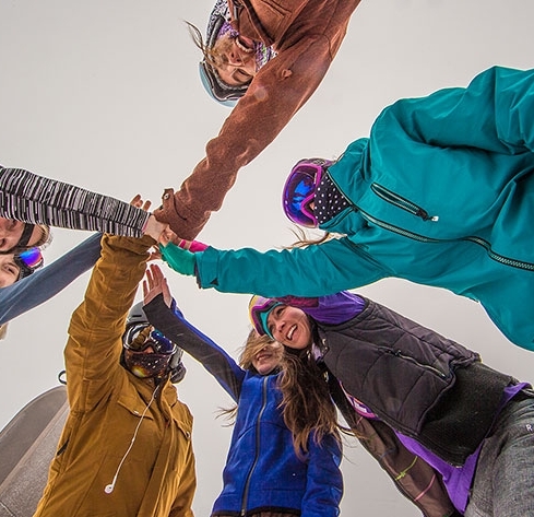 7 FEMALE SKIER AND SNOWBOARDERS WITH HANDS TOGETHER IN THE MIDDEL