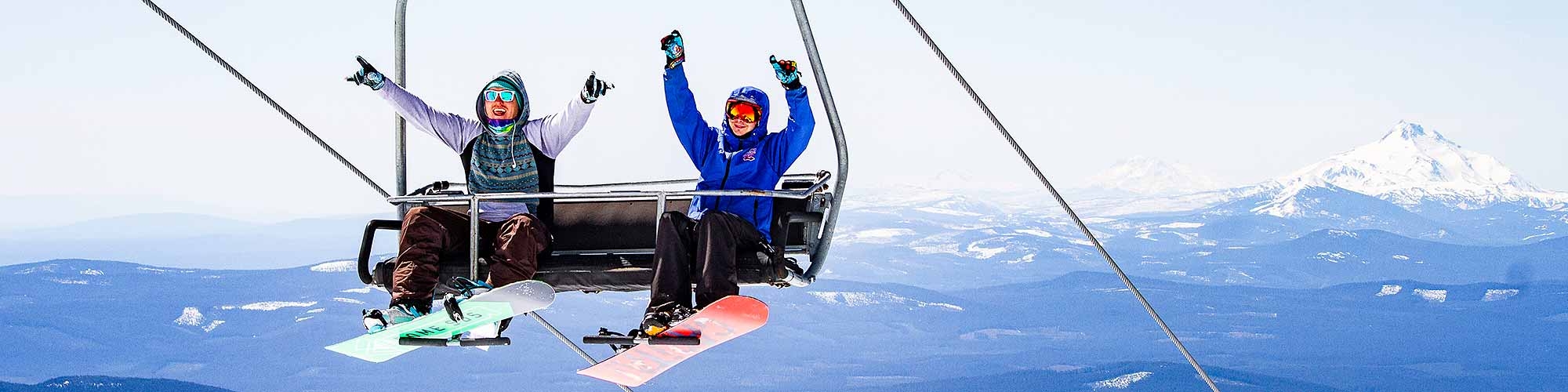 TWO HAPPY SNOWBOARDERS ON LIFT WITH MT. JEFFERSON IN BACKGROUND