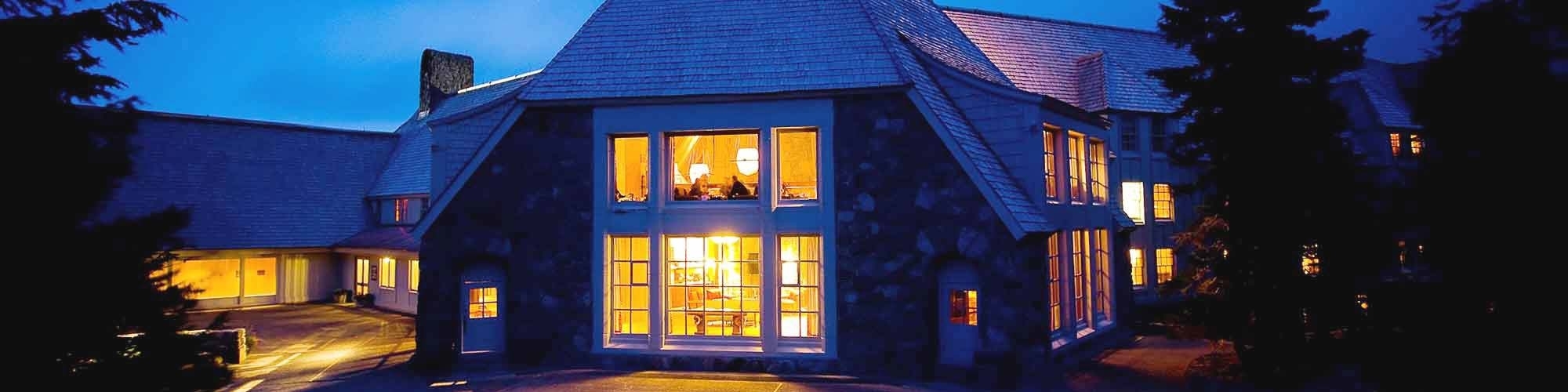 DUSK VIEW FROM BACK PATIO INTO WELL-LIT LODGE WINDOWS