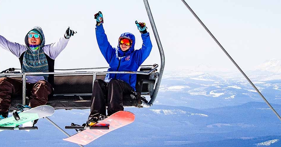 TWO HAPPY SNOWBOARDERS ON LIFT WITH MT. JEFFERSON IN BACKGROUND