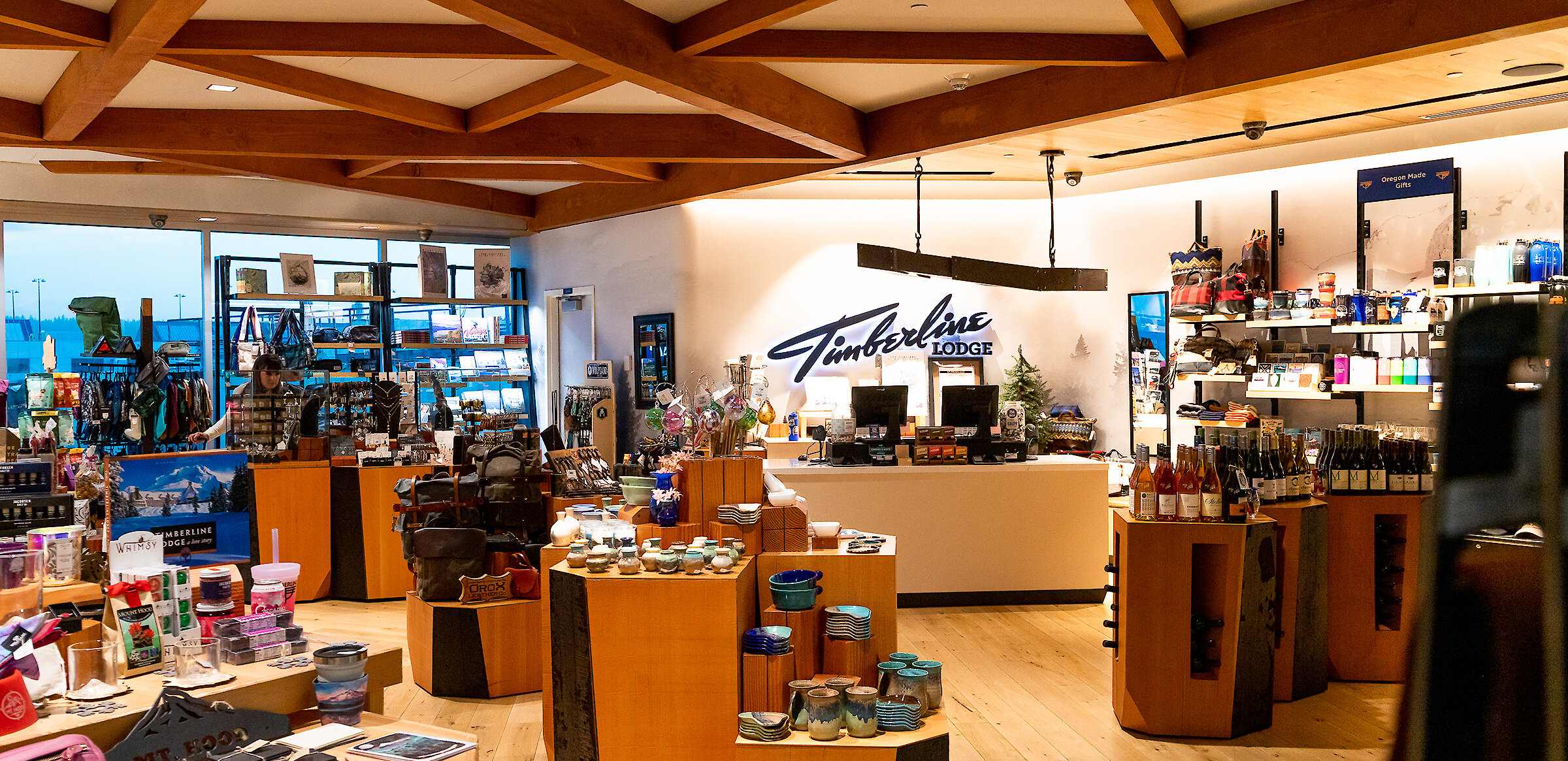 Interior of the Timberline Lodge store at Portland International Airport, featuring wooden displays with pottery, souvenirs, apparel, and Oregon-made gifts under warm lighting and a Timberline Lodge sign behind the counter.